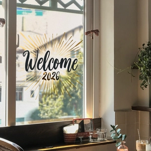 Detail of Welcome 2026 black calligraphy and gold rays on glass window sticker