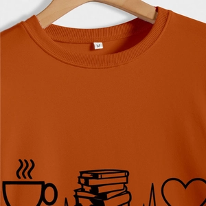 Close-up of orange crewneck sweatshirt showing the tea, books, and heart printed design