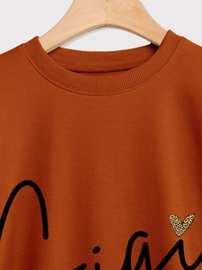 Détail du col rond et de l'imprimé cœur léopard sur un sweat orange surdimensionné