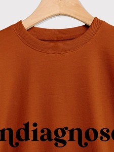 Detail eines karamellfarbenen Sweatshirts mit Vintage-Buchstabendruck am Ausschnitt