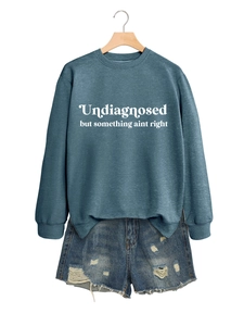 Detail eines blaugrauen Sweatshirts mit Text auf Holzbügel und Jeansshorts für Damen