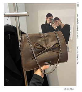Detail of brown PU leather shoulder bag with bow decor and silver metal chain strap
