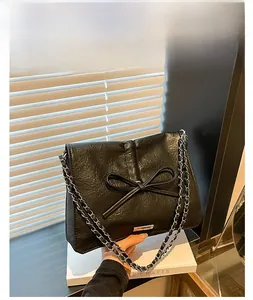 Detail of black bow shoulder bag featuring a crinkled texture and woven chain strap