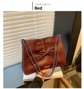 Detail view of burgundy tote bag featuring a leather bow and silver chain strap
