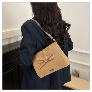 Detail of khaki leather tote with bow decoration and metal chain strap shown on model
