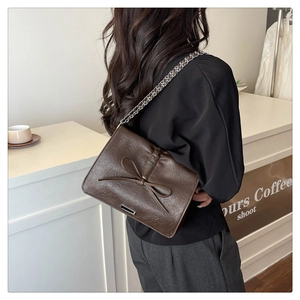 Detail of dark brown bow shoulder bag with silver chain strap shown on a model