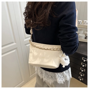 Détail du sac seau crème avec chaîne dorée et peluche porté par le mannequin