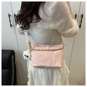 Detail of pink shoulder bag featuring textured fabric and gold chain with plush pendant