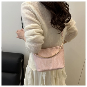 Sac seau rose pâle avec chaîne dorée porté par un mannequin dans un cadre épuré