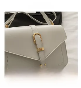 Détail d'un sac blanc avec rabat en V et fermoir métallique doré sur le devant du sac