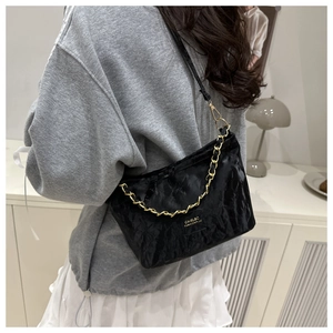 Close-up of black hobo bag with glossy pleated texture and gold chain strap detail