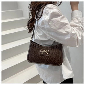 Close-up of crocodile pattern leather underarm bag with gold bow clasp on a shoulder