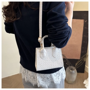 Detail view of white mini handbag with crocodile pattern texture and gold hardware