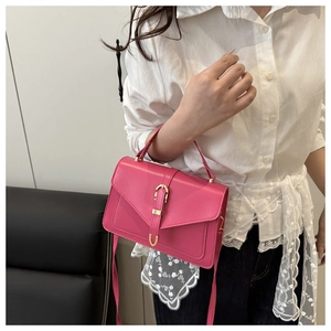 Detail of rose pink handbag with gold hardware and textured leather worn by model