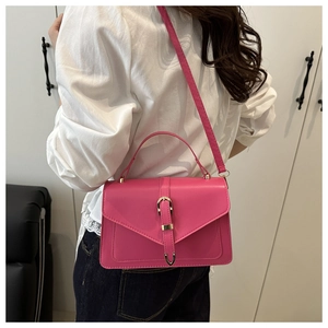 Detail view of pink crossbody bag with metal buckle strap worn by a female model