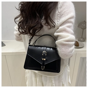 Détail d'un sac bandoulière en cuir noir avec ferrures dorées porté par un mannequin