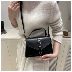 Elegant black crossbody bag with V-shaped flap and gold hardware on a white knit sweater