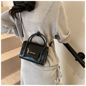 Detail of a black patent leather crossbody bag with a gold Fashion & Bags logo engraving