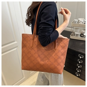 Close-up of brown faux leather tote bag featuring detailed floral embossing and metal logo