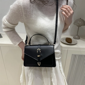 Structured black leather handbag with gold hardware on a model in a minimalist setting