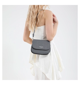 Detail of dark grey saddle bag with leather texture and white fashion slogan on white dress