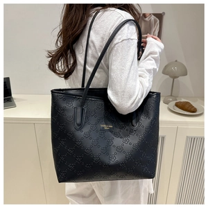 Detail of black tote bag featuring embossed floral patterns and metal fashion logo