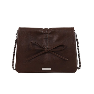 Retro dark brown shoulder bag with leather bow detail and metal plaque on white background