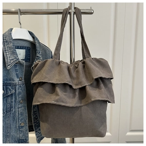 Detail of grey ruffled tote bag in faux suede fabric hanging on a chrome metal hanger