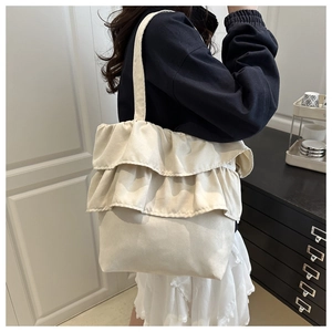 Detail of beige canvas tote bag with multi-layer ruffle design and shoulder strap
