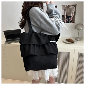 Detail of black ruffled canvas tote bag with layered pleats shown in a lifestyle indoor setting