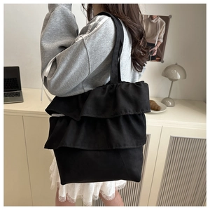 Detail of black ruffled tote bag showing layered pleats on textured canvas fabric