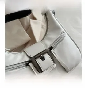 Detailed close-up of beige leather crescent bag with bronze buckle and long zipper pulls