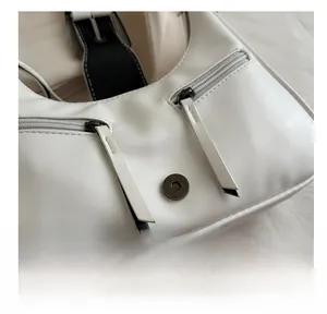 Detail view of a white leather bag featuring a silver metal zipper and magnetic buckle