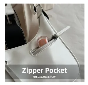Detail of white leather crescent bag featuring a functional front zipper pocket for lipstick