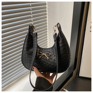 Close-up of woven black leather texture and gold bow detail on crescent shoulder bag