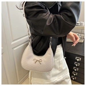 Close-up of white crescent shoulder bag with crocodile pattern and golden bow buckle detail