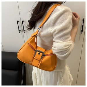 On-shoulder view of orange leather underarm bag with silver buckle and side zippers