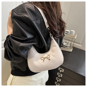 Detail of ivory crescent shoulder bag featuring crocodile embossed texture and gold bow