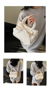 Detail of cream tote bag with large bow decoration, gold lettering and dual strap options