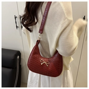 Detail of burgundy crescent shoulder bag with woven texture and gold bow buckle clasp
