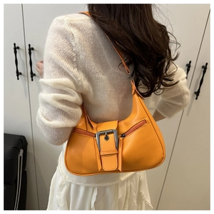 Detail of hobo bag in orange leather featuring a silver buckle on a white knit sweater