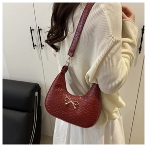 Detail of a dark red woven crescent shoulder bag with a gold bow buckle on a model