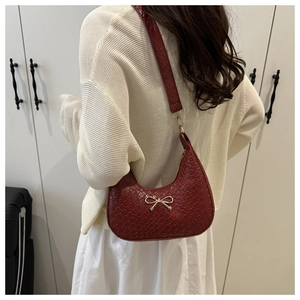 Detail of burgundy hobo bag with woven texture and gold bow buckle on white sweater