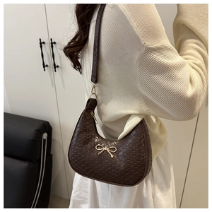 Close-up of a dark brown crescent underarm bag with crocodile pattern and metal bow