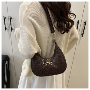Detail of dark brown woven underarm bag featuring a golden bow metal accessory