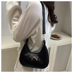 Detail of black croc-embossed crescent shoulder bag with golden bow buckle on model