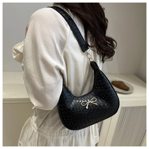 Close-up of black crocodile pattern hobo bag with a gold bow buckle on white dress