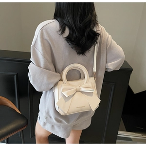 Close-up of cream white leather handbag with a large decorative bow and shoulder strap