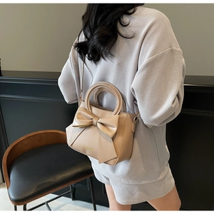 Beige crossbody bag featuring a large decorative bow and elegant fashion lettering