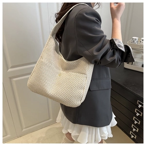 Détail d'un grand sac seau tissé crème porté à l'épaule dans une pièce minimaliste